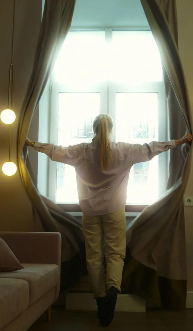 Mujer abriendo una ventana para que ingrese luz natural para ahorrar energía. Fuente: Pexels